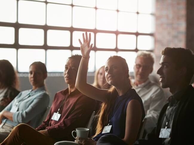 Businesswoman with raised hand at convention in New York style auditorium