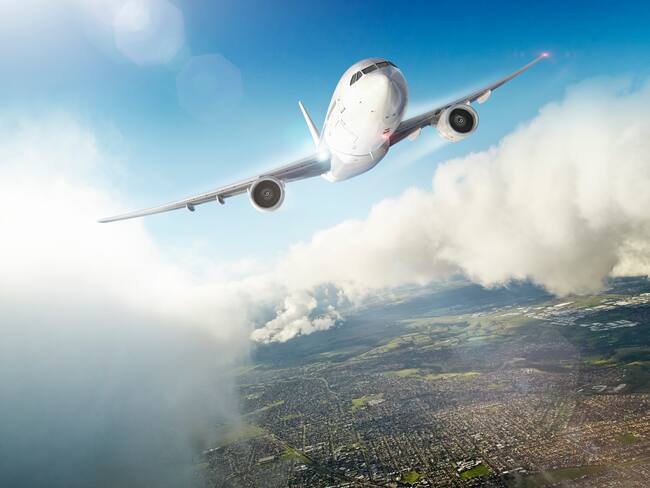 Avión volando sobre una ciudad y atravesando las nubes (Foto vía GettyImages)