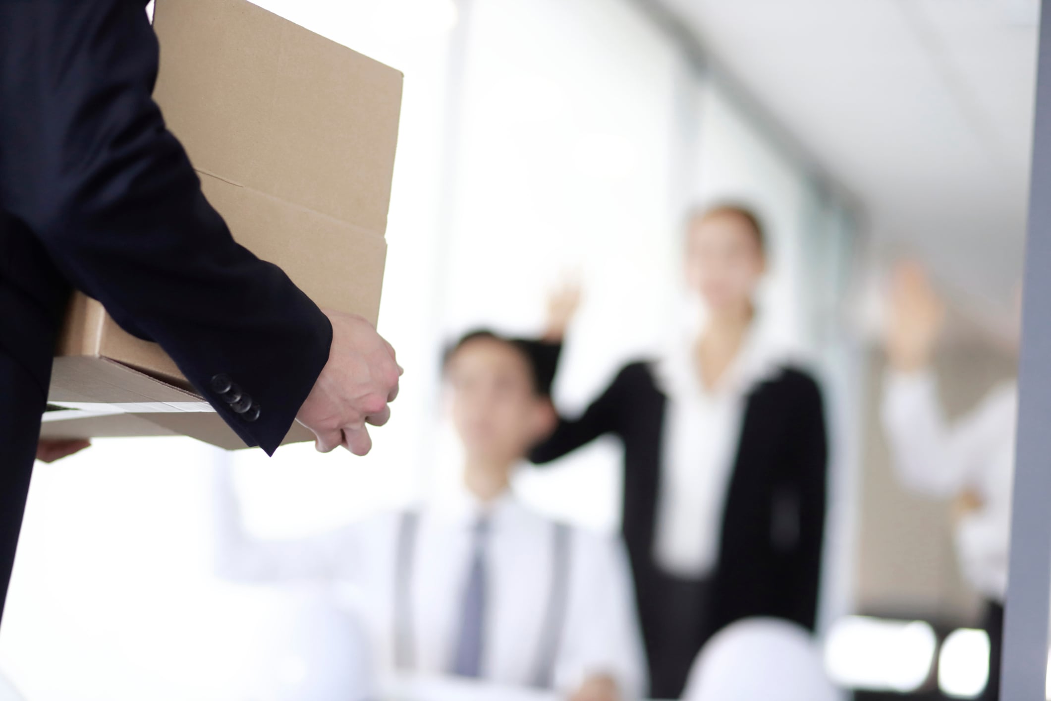 Hombre cargando una caja, mientras al fondo se despiden de él en el trabajo (Getty Images)