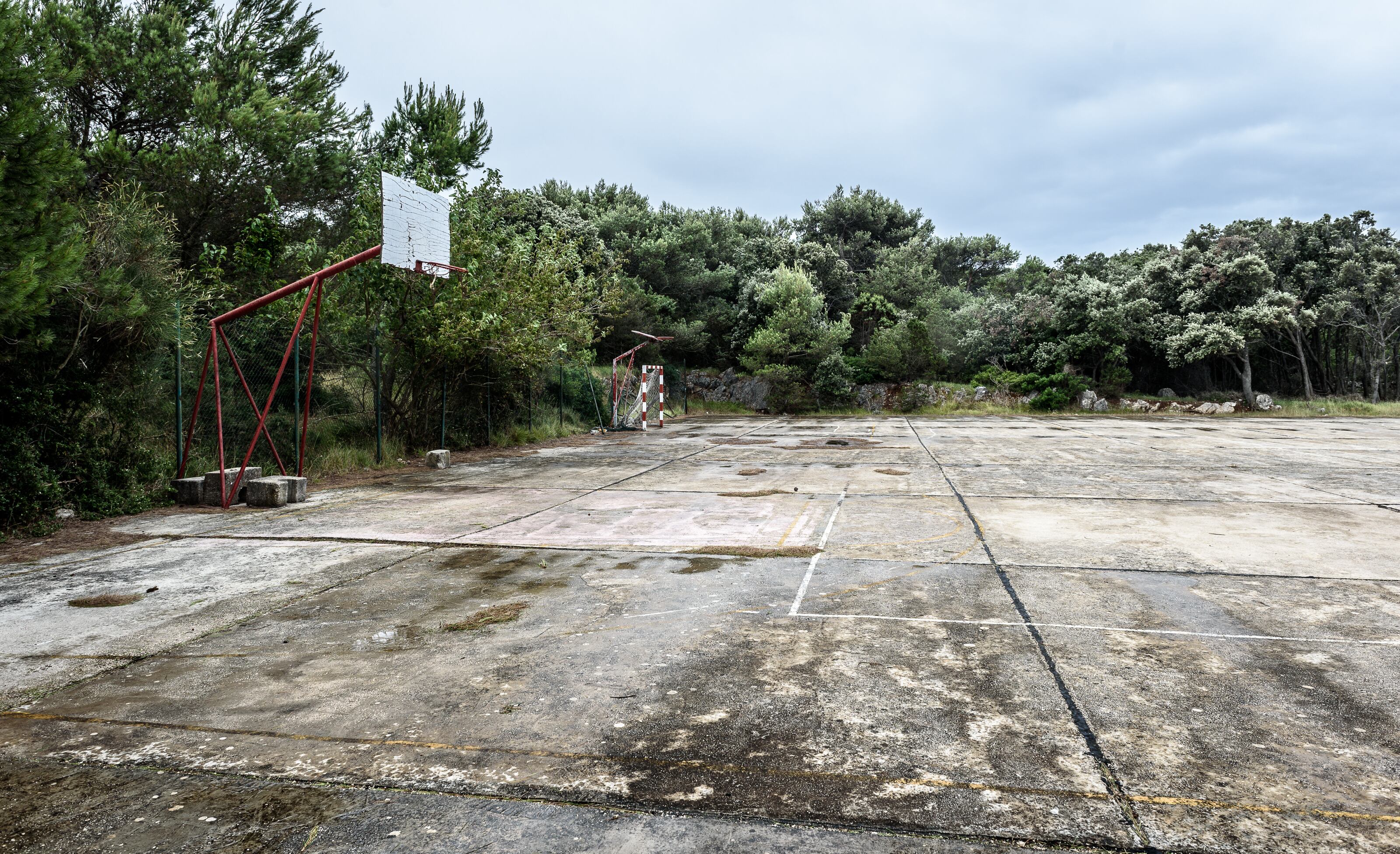Old abandoned school sports court or schoolyard for different activities. Ruins of a sport venue abandoned long time ago with soccer, handball or football goals, basketball hoops and boards and destroyed concrete plates.