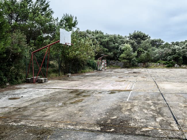 Old abandoned school sports court or schoolyard for different activities. Ruins of a sport venue abandoned long time ago with soccer, handball or football goals, basketball hoops and boards and destroyed concrete plates.