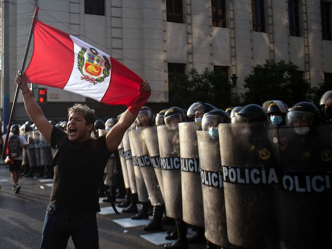 A demonstrator stands in front of riot police members during a protest against the governement of Peru's President Pedro Castillo, in Lima on April 05, 2022 - Peruvian President Pedro Castillo announced the end of a curfew in the capital Lima aimed at containing protests against rising fuel prices following crisis talks with Congress. (Photo by ERNESTO BENAVIDES / AFP) (Photo by ERNESTO BENAVIDES/AFP via Getty Images)