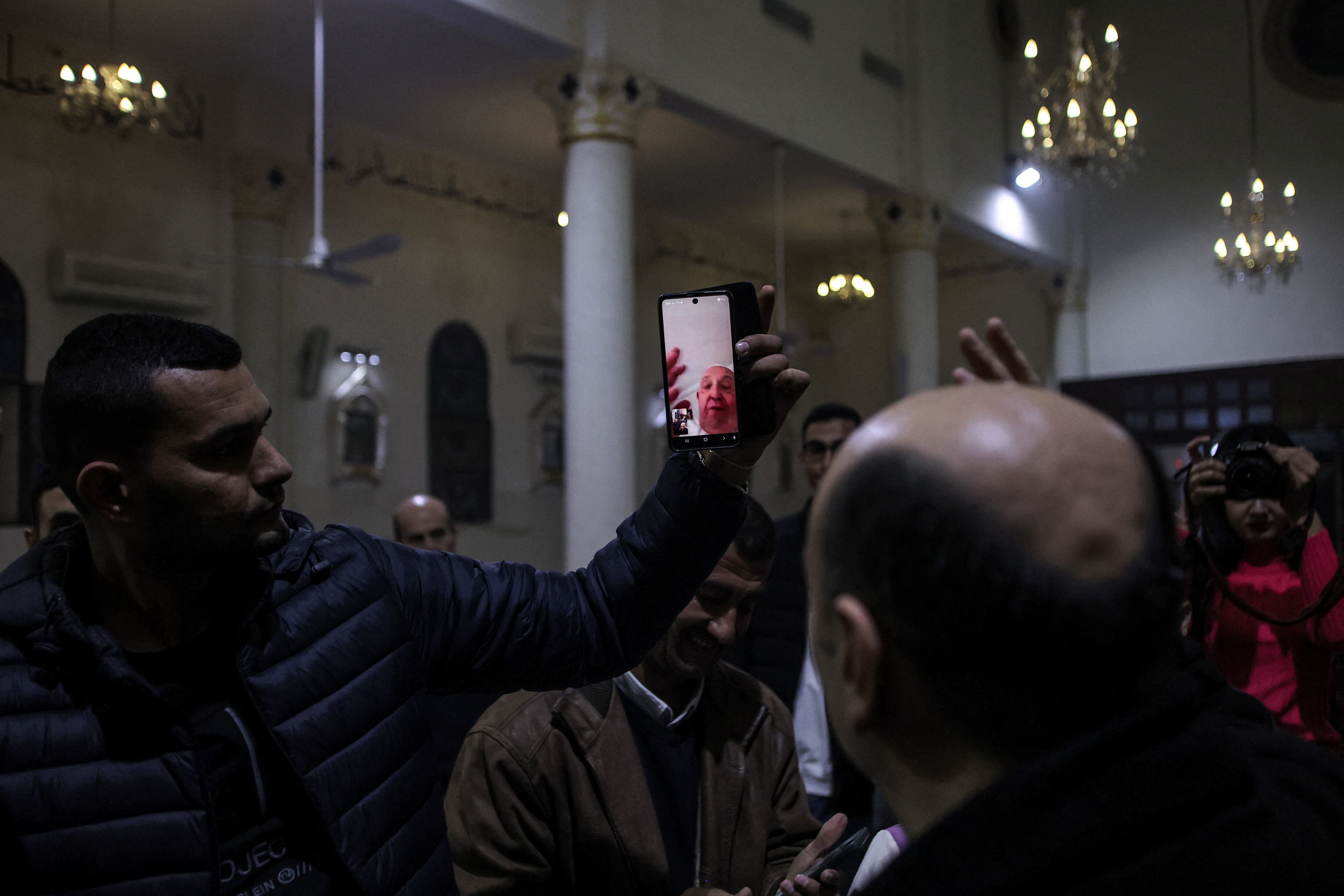 Un hombre sostiene un teléfono para que el padre Gabriel Romanelli, párroco de la iglesia católica romana de la Sagrada Familia, mantenga una videoconferencia con el papa Francisco, el 24 de diciembre de 2024. AFP vía Getty Images