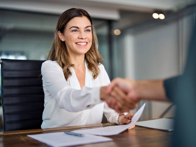 Mujer sonríe y estrecha la mano de un contratista tras conseguir empleo