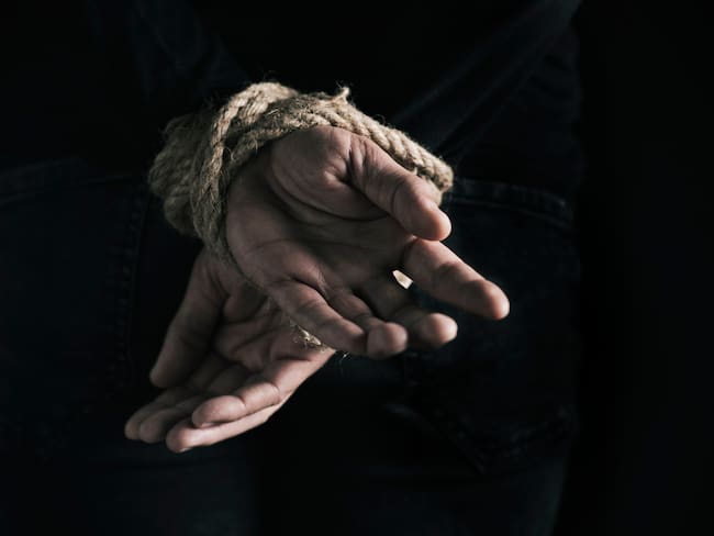 closeup rear view of a man with his hands tied behind his back with rope, against a black background
