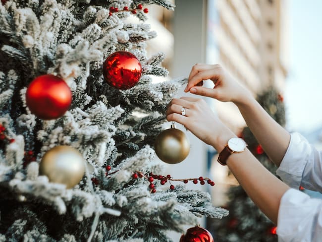 Cropped hand of woman decorating and hanging baubles on Christmas tree