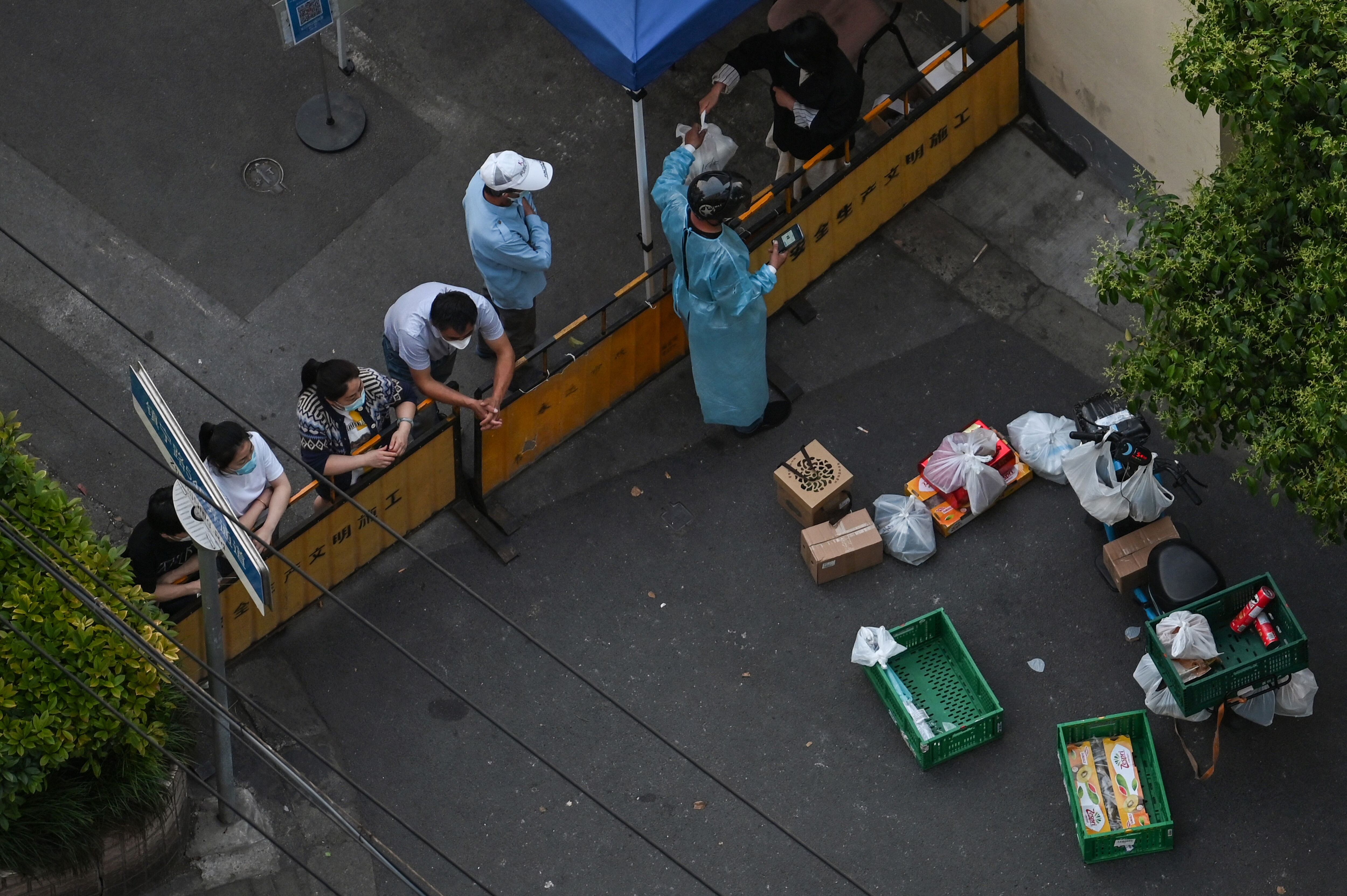A resident collects food from a delivery worker at a checkpoint on a street during a Covid-19 coronavirus lockdown in the Jing'an district in Shanghai on May 17, 2022. (Photo by Hector RETAMAL / AFP) (Photo by HECTOR RETAMAL/AFP via Getty Images)