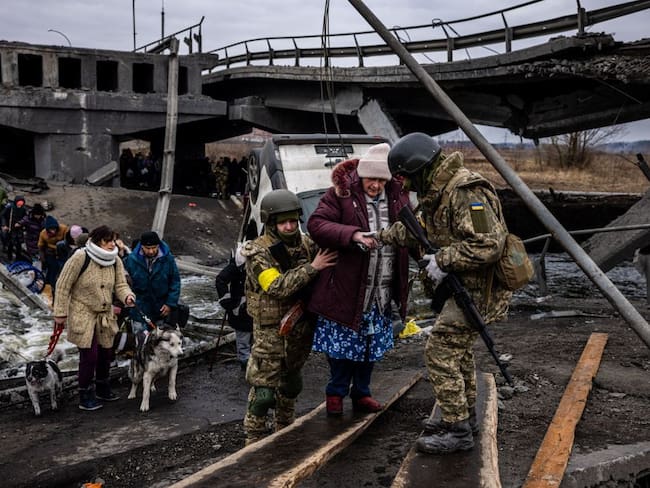 Soldados ucranianos ayudan a una anciana a cruzar un puente destruido mientras evacua la ciudad de Irpin, al noroeste de Kiev (Photo by Dimitar DILKOFF / AFP) (Photo by DIMITAR DILKOFF/AFP via Getty Images)