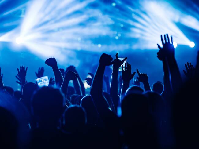 Silhouettes of people rising their hands and dancing on an open air music festival. There are blue stage lights. People having fun at rock concert on a summer music festival.