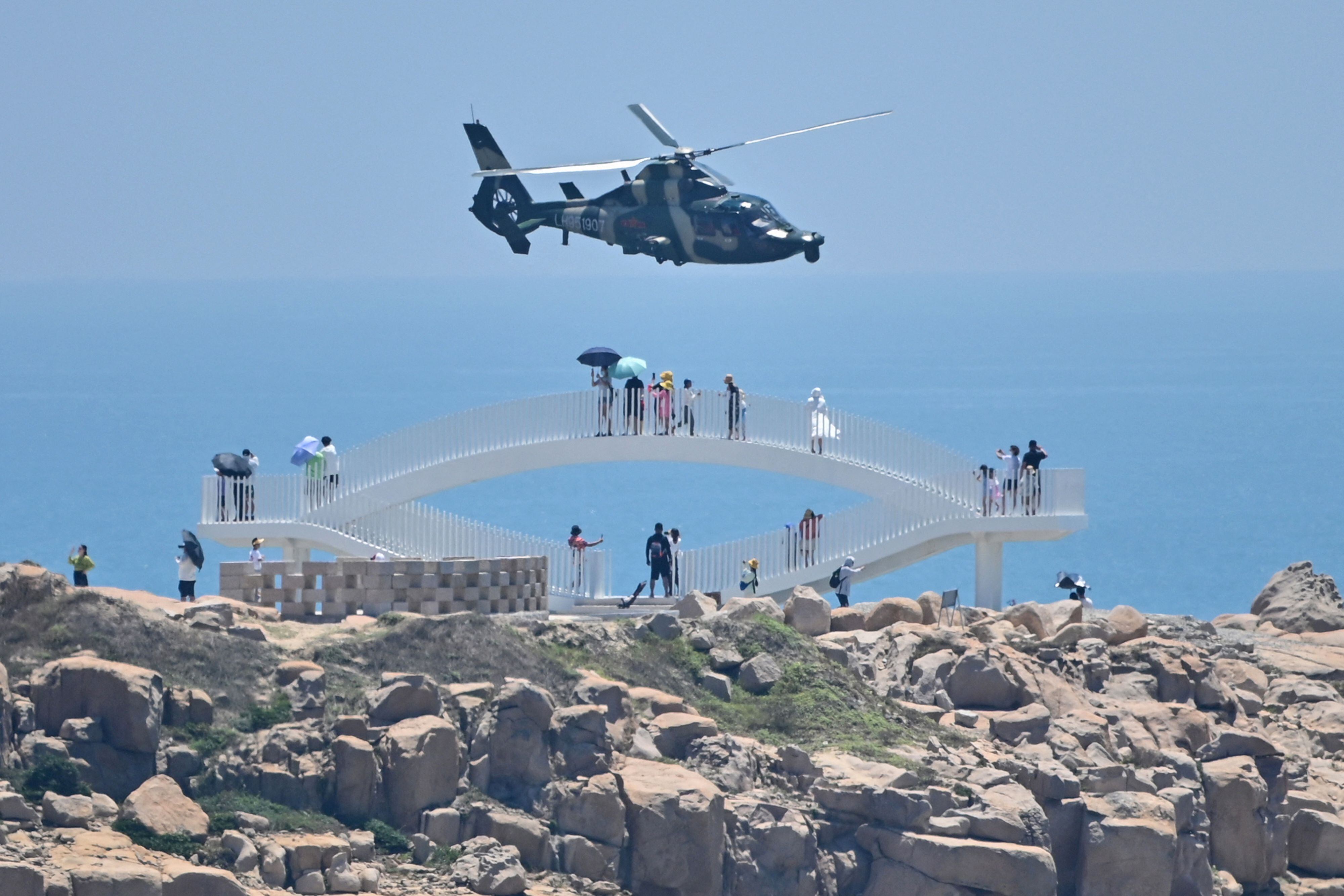 Turistas observan cómo un helicóptero militar chino vuela más allá de la isla de Pingtan, uno de los puntos más cercanos de China continental a Taiwán. 4 de agosto de 2022. (Photo by HECTOR RETAMAL/AFP via Getty Images)