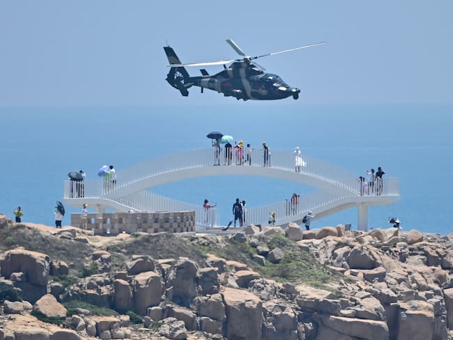 Turistas observan cómo un helicóptero militar chino vuela más allá de la isla de Pingtan, uno de los puntos más cercanos de China continental a Taiwán. 4 de agosto de 2022. (Photo by HECTOR RETAMAL/AFP via Getty Images)
