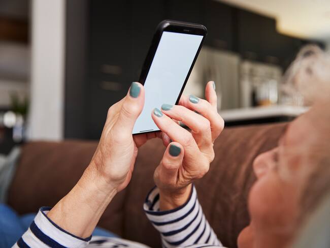 Senior woman lying on couch using smartphone, close up