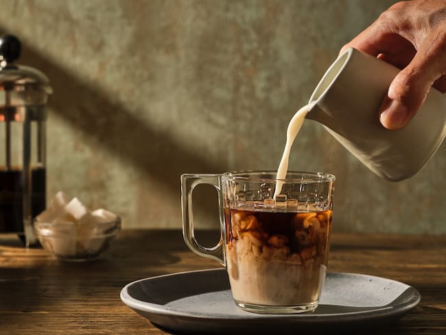 Persona vertiendo leche en una taza de café / Foto: GettyImages