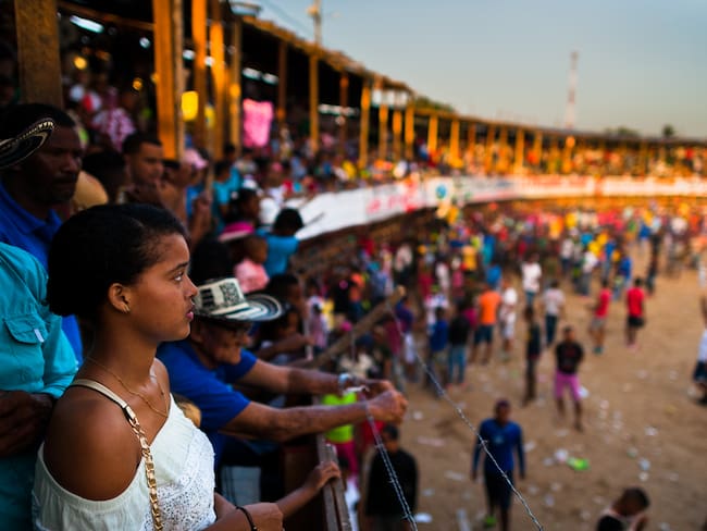 SOPLAVIENTO, COLOMBIA - DECEMBER 17: A young Colombian woman looks down at the amateur bullfighters in the arena of a 'Corraleja' bullfighting festival on December 17, 2017 in Soplaviento, Colombia. Amateur bullfights known as 'Corralejas' take place in villages and towns on the Caribbean coast of Colombia. Families and people from all around meet on wooden bleachers of a temporarily built bullring to eat, drink and watch hundreds of amateur bullfighters risking their lives, taunting bulls, and showing their masculinity and courage in the arena. Unlike the corrida, the bulls in 'Corralejas' are never killed. (Photo by Jan Sochor/Getty Images)