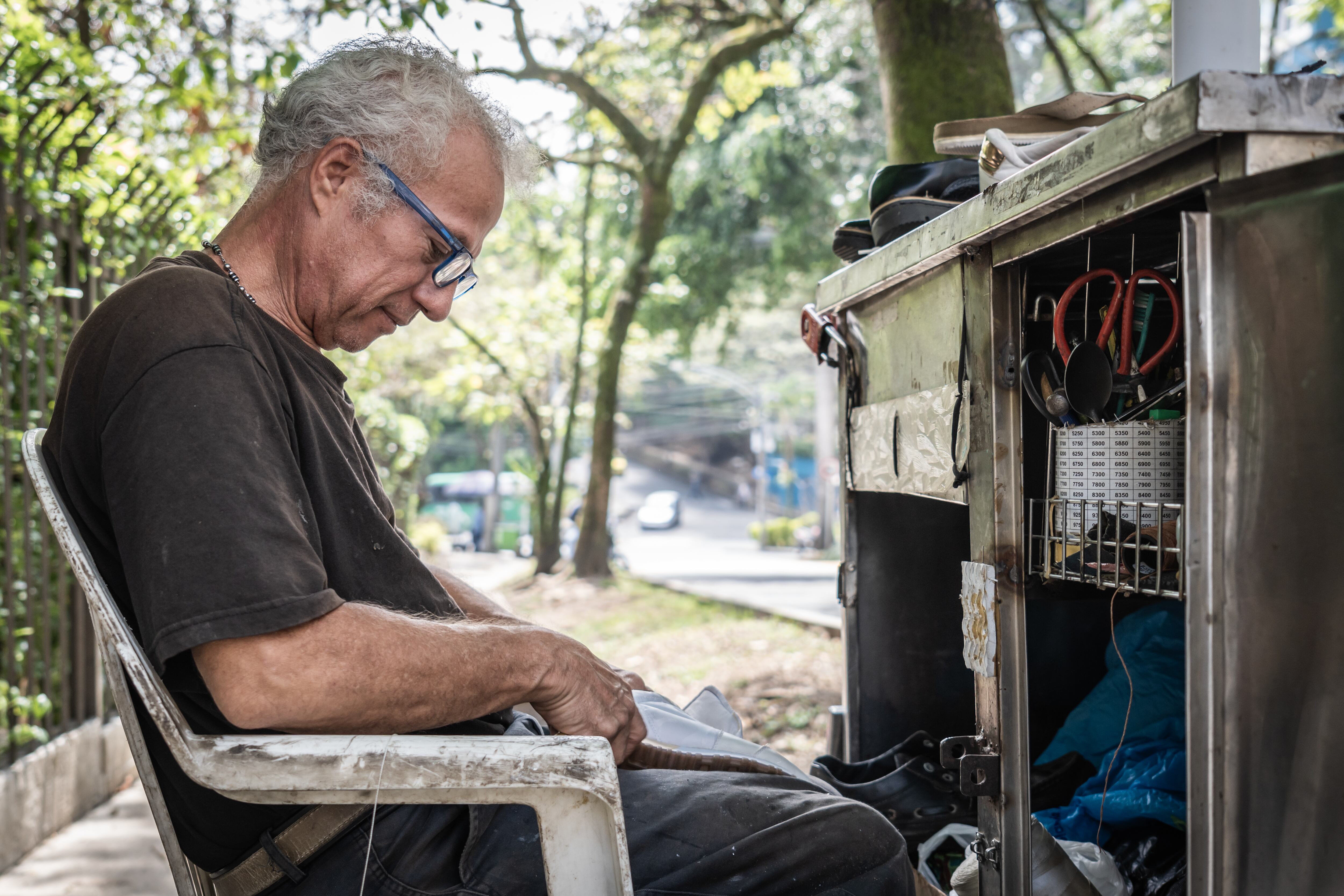 Un hombre mayor, trabajador independiente, remienda zapatos sentado al aire libre en una pequeña estación de trabajo. Getty Images.