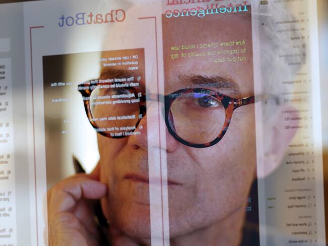 Close up stock photograph of a mature man studying a see-through computer monitor that’s displaying text provided by an AI (artificial intelligence) chatbot.