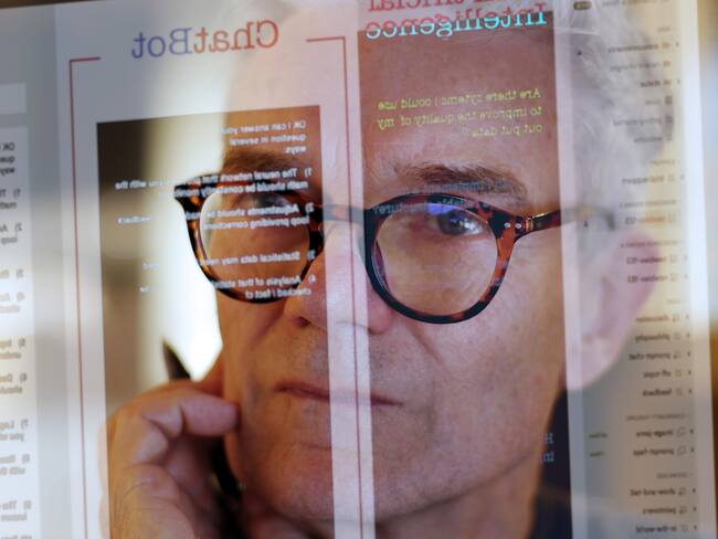Close up stock photograph of a mature man studying a see-through computer monitor that’s displaying text provided by an AI (artificial intelligence) chatbot.