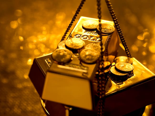 Lingote de oro entre monedas sobre una pesa (Getty Images)