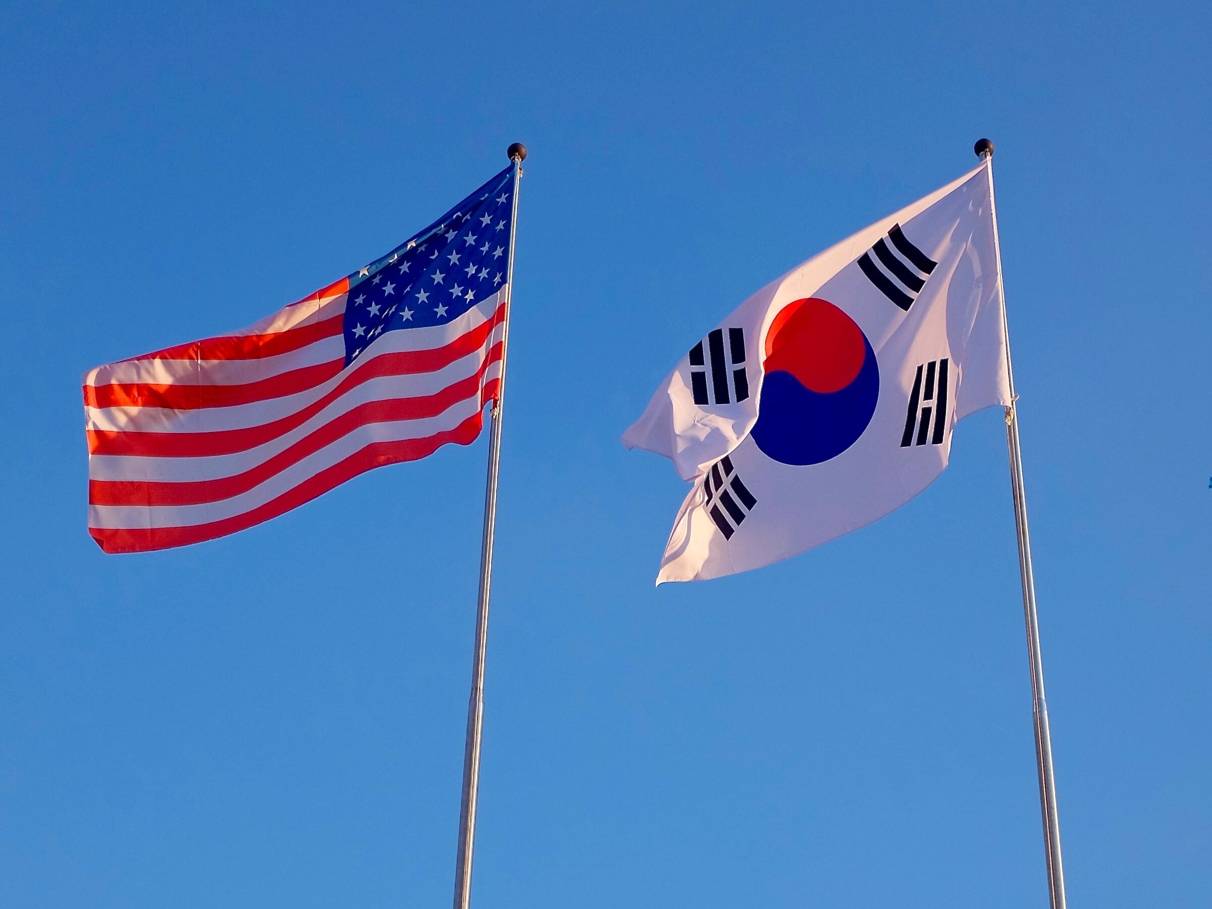 Flags of the United States and South Korea (Republic of Korea), against a blue sky.