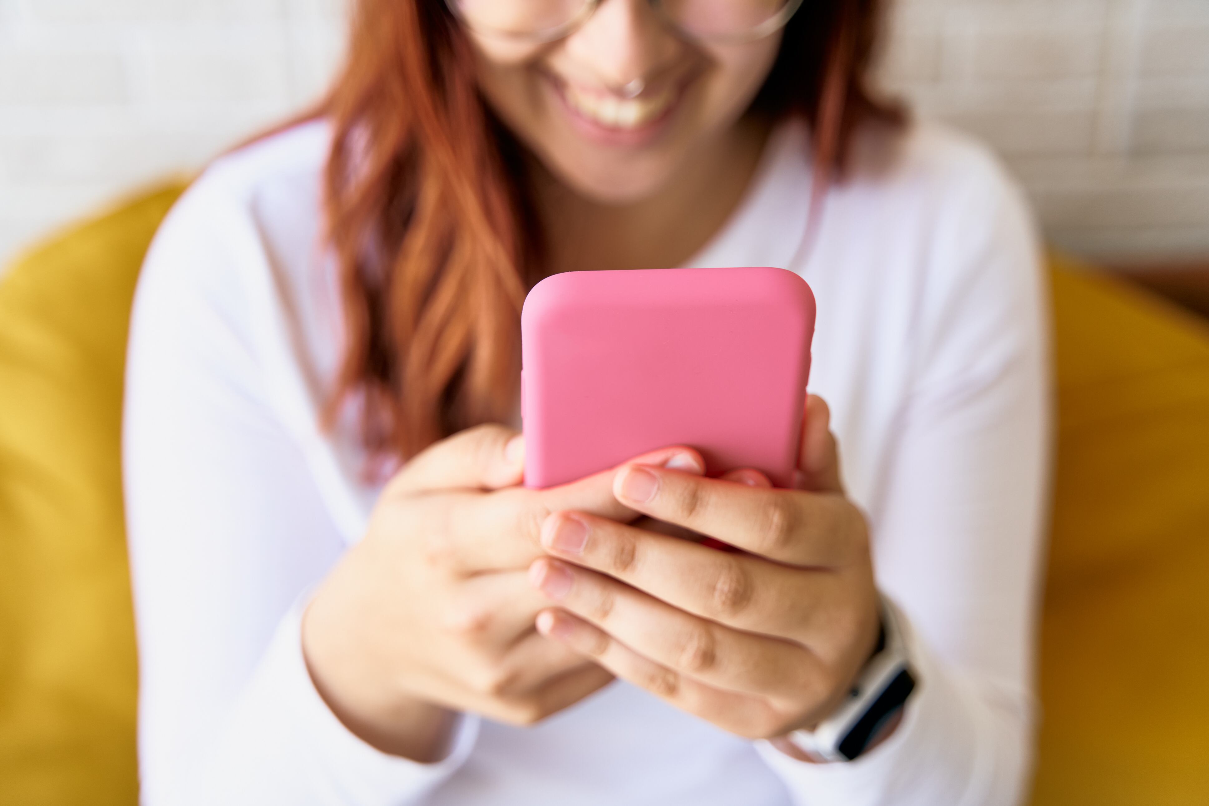 Mujer de camisa blanca utilizando aplicaciones en su celular mientras sonríe (Foto vía Getty Images)