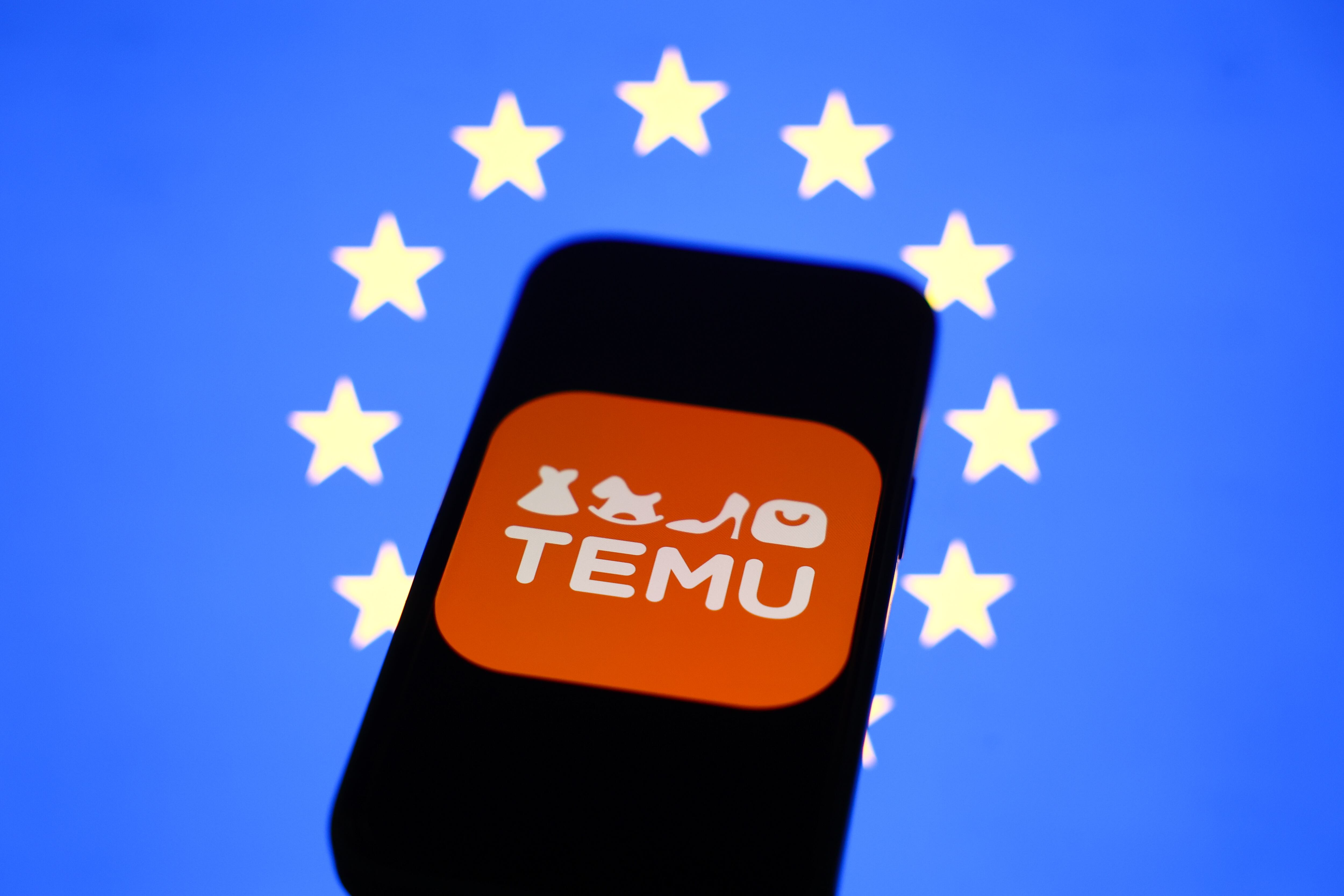 Logo de Temu con bandera de la Unión Europea de fondo. FOTO: Jakub Porzycki/NurPhoto via Getty Images