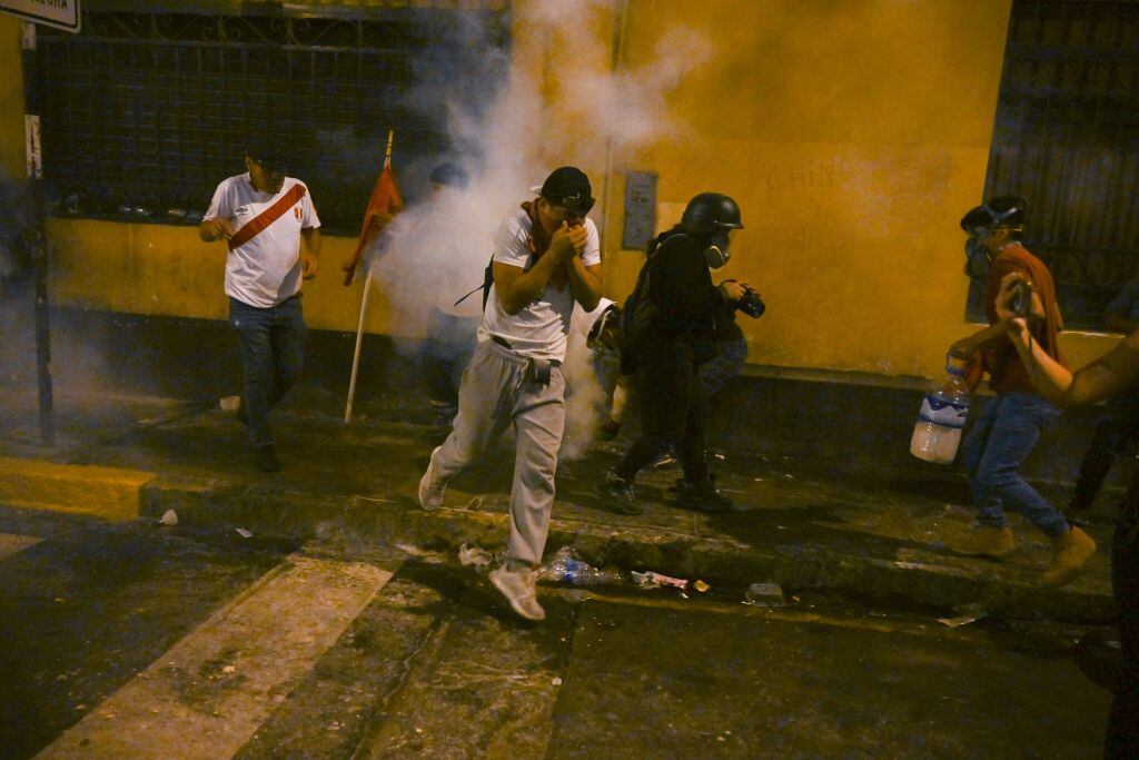People take cover from tear gas during a protest against the government of President Dina Boluarte in Lima on January 19, 2023. - Thousands of protesters began marching through Peru's capital Thursday to demand the president's resignation and fresh elections, following weeks of violent unrest that have left 44 people dead. (Photo by ERNESTO BENAVIDES / AFP) (Photo by ERNESTO BENAVIDES/AFP via Getty Images)