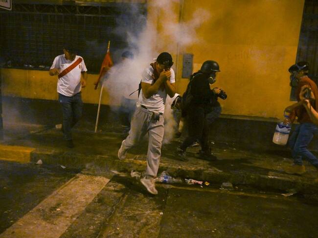 People take cover from tear gas during a protest against the government of President Dina Boluarte in Lima on January 19, 2023. - Thousands of protesters began marching through Peru's capital Thursday to demand the president's resignation and fresh elections, following weeks of violent unrest that have left 44 people dead. (Photo by ERNESTO BENAVIDES / AFP) (Photo by ERNESTO BENAVIDES/AFP via Getty Images)