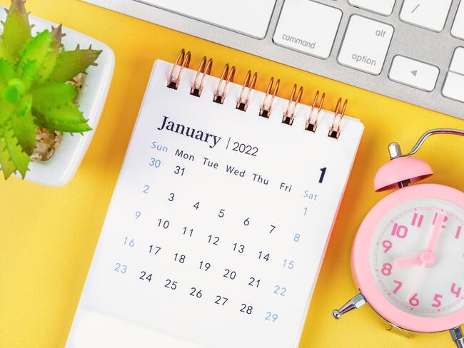 January 2022 desk calendar and pink alarm clock with keyboard computer.