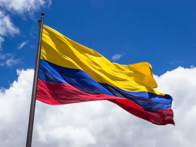 Horizontal shot of the colombian flag being move by the wind over sky and clouds on a sunny day.