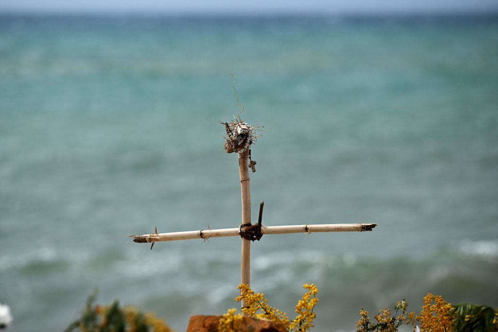 This photograph taken on March 9, 2023, shows a view of a bamboo cross with a rosary, set as a memorial on a beach near Cutro, with the Mediterranean Sea in the background, where at least 72 migrants died on February 26, after their boat sank off Italy's southern Calabria region. - Italian Prime Minister will hold a cabinet meeting on March 9 near the site of a deadly shipwreck, as the debate rages over whether the right-wing government's migration policies cost lives. (Photo by Tiziana FABI / AFP) (Photo by TIZIANA FABI/AFP via Getty Images)
