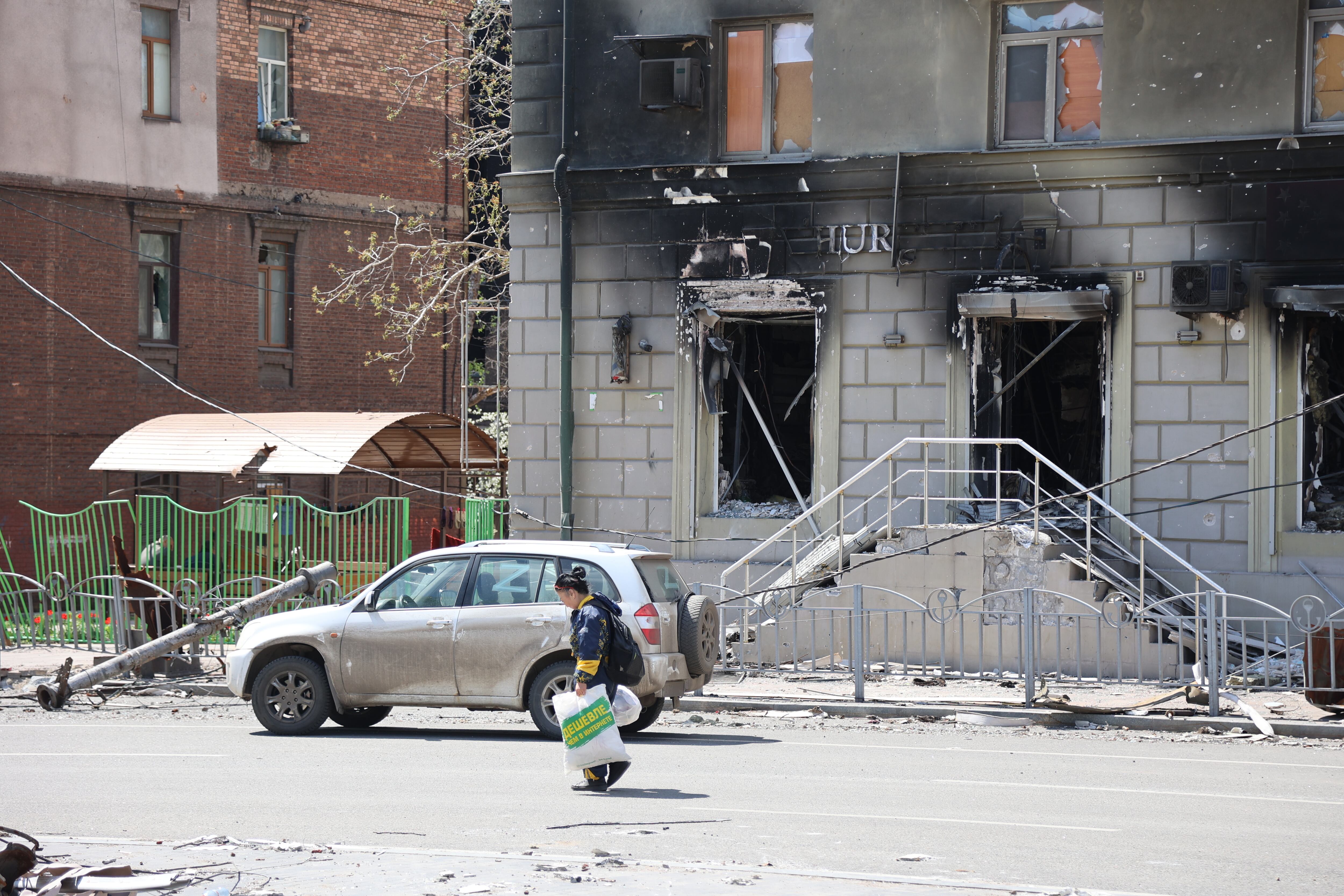 MARIUPOL, UKRAINE - APRIL 27: A woman walks past a burnt building in Ukrainian city of Mariupol under the control of Russian military and pro-Russian separatists, on April 27, 2022. Townspeople began to organize themselves, clean up garbage and rubble. Volunteers continue their efforts to deliver humanitarian aid to people. (Photo by Leon Klein/Anadolu Agency via Getty Images)