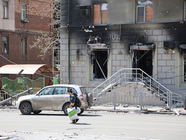 MARIUPOL, UKRAINE - APRIL 27: A woman walks past a burnt building in Ukrainian city of Mariupol under the control of Russian military and pro-Russian separatists, on April 27, 2022. Townspeople began to organize themselves, clean up garbage and rubble. Volunteers continue their efforts to deliver humanitarian aid to people. (Photo by Leon Klein/Anadolu Agency via Getty Images)