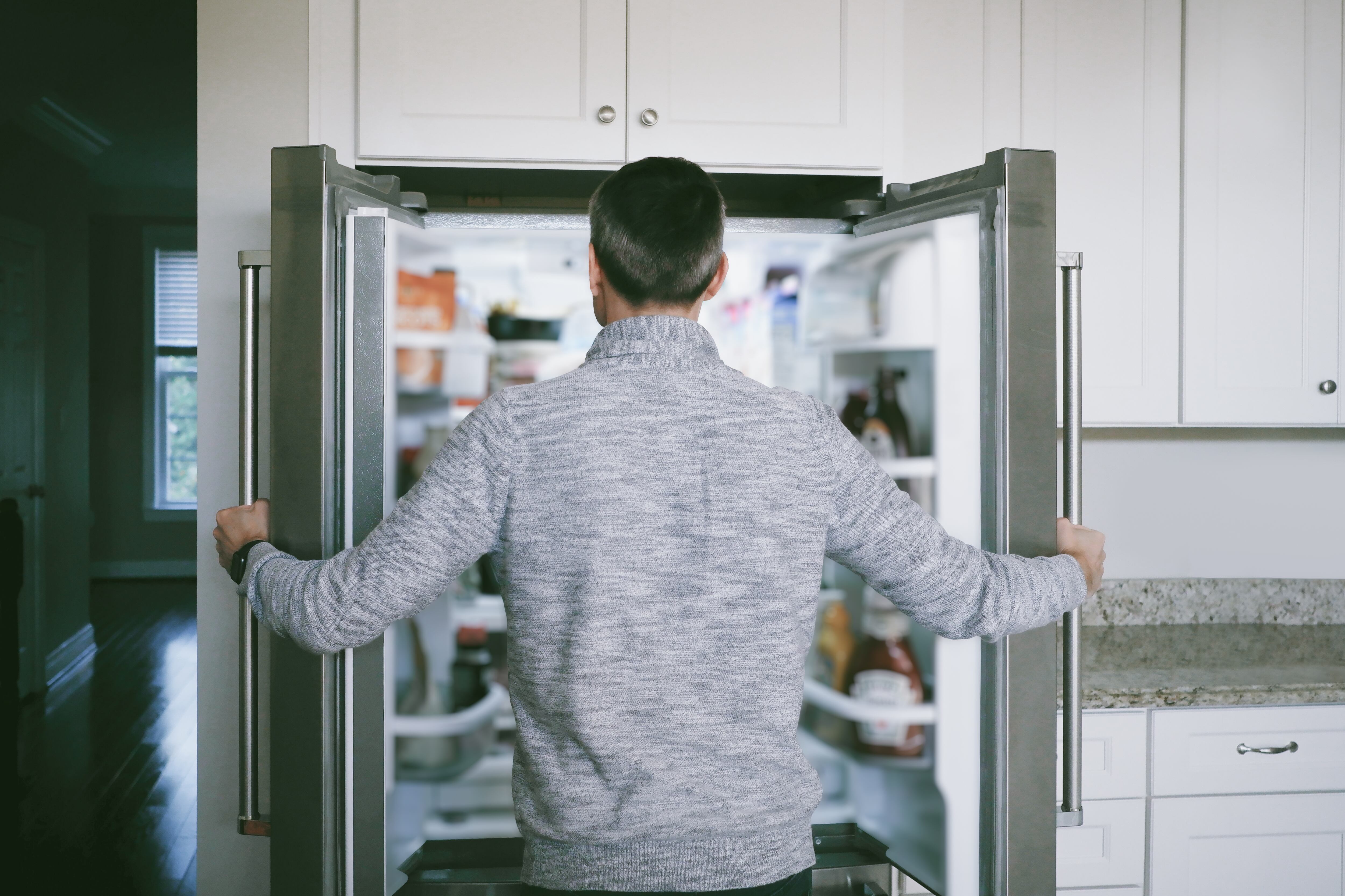 Hombre abriendo las puertas de su nevera para buscar comida (Foto vía GettyImages)