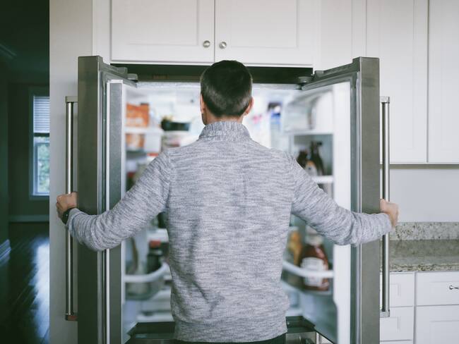 Hombre abriendo las puertas de su nevera para buscar comida (Foto vía GettyImages)