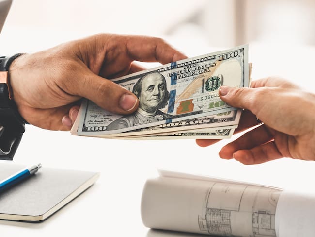 Persona entregando un monto de dinero en dólares estadounidenses a otra persona (Foto vía Getty Images)