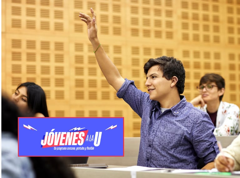 Joven en un salón de clase universitario, levantando la mano / Jóvenes a la U (Getty Images)