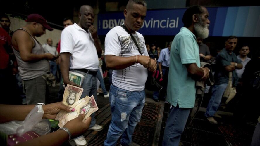 Una mujer cuenta sus billetes de 100 bolívares mientras hace fila fuera de un banco en Caracas. Foto: Associated Press - AP