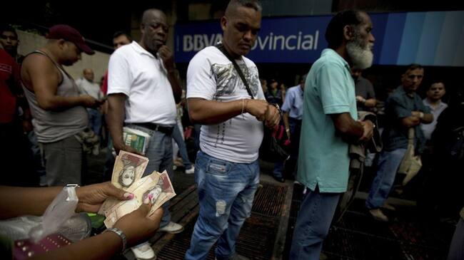 Una mujer cuenta sus billetes de 100 bolívares mientras hace fila fuera de un banco en Caracas. Foto: Associated Press - AP