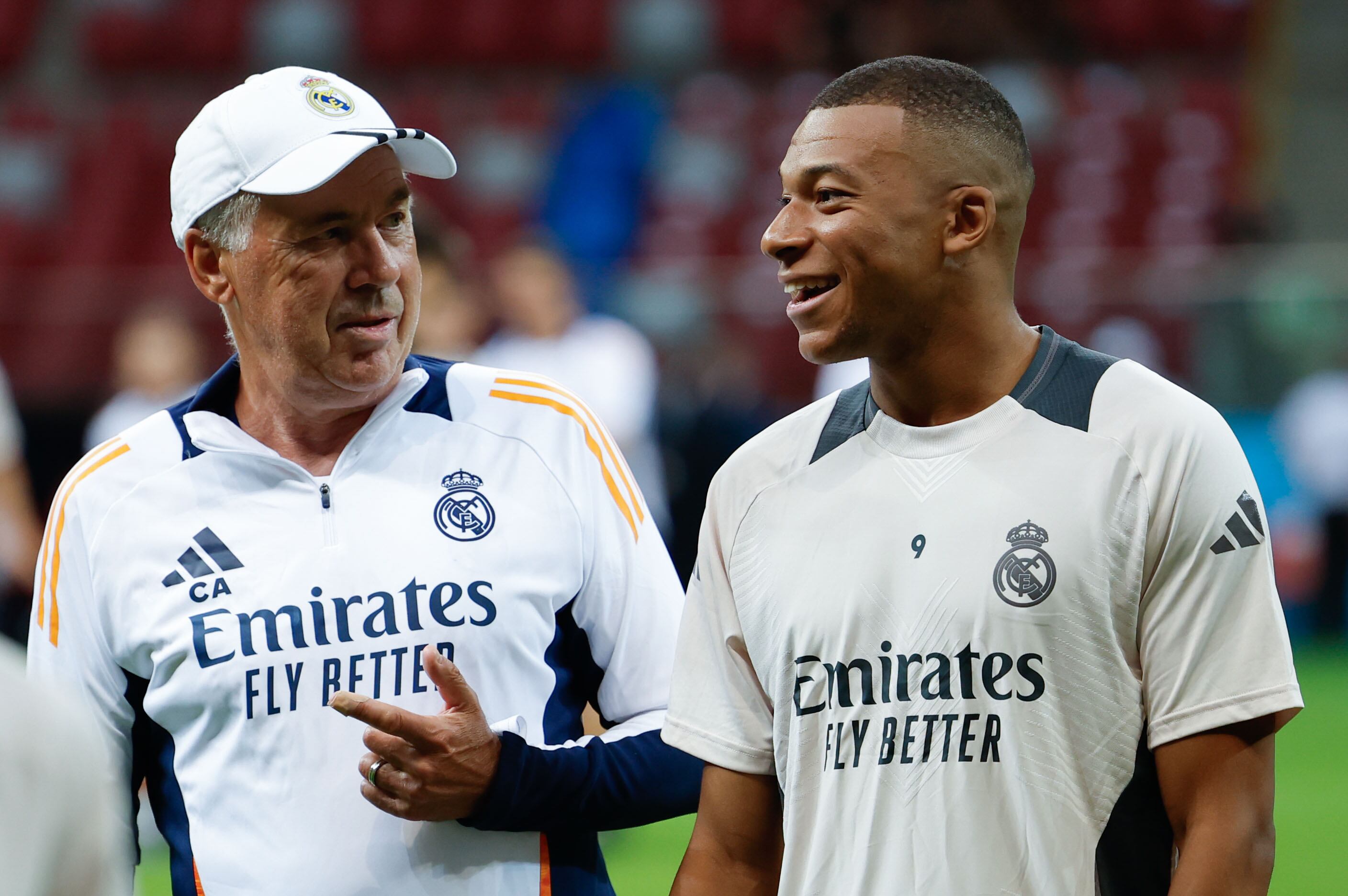 El nuevo delantero del Real Madrid, el francés Kylian Mbappé (d) recibe instrucciones de su entrenador, el italiano Carlo Ancelotti, en el entrenamiento del equipo este martes en Varsovia, en la víspera del partido de la Supercopa de Europa de fútbol. Foto: EFE.