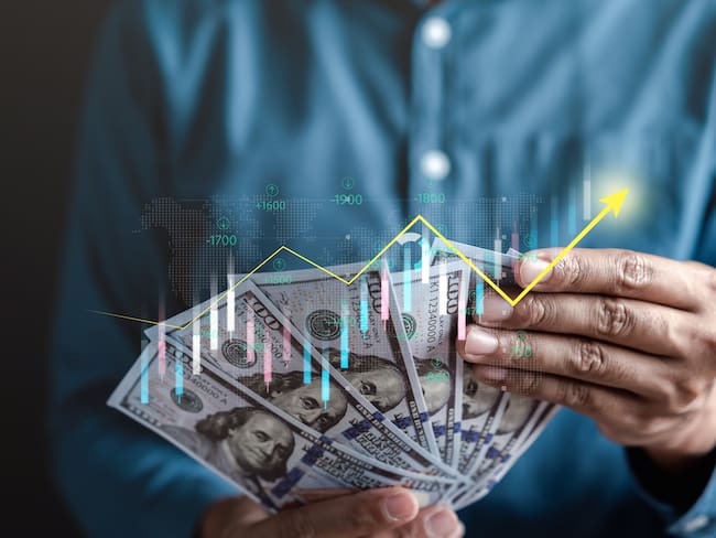 Hombre de negocios contando dólares mientras se refleja gráfica sobre los aumentos de la divisa (Getty Images)