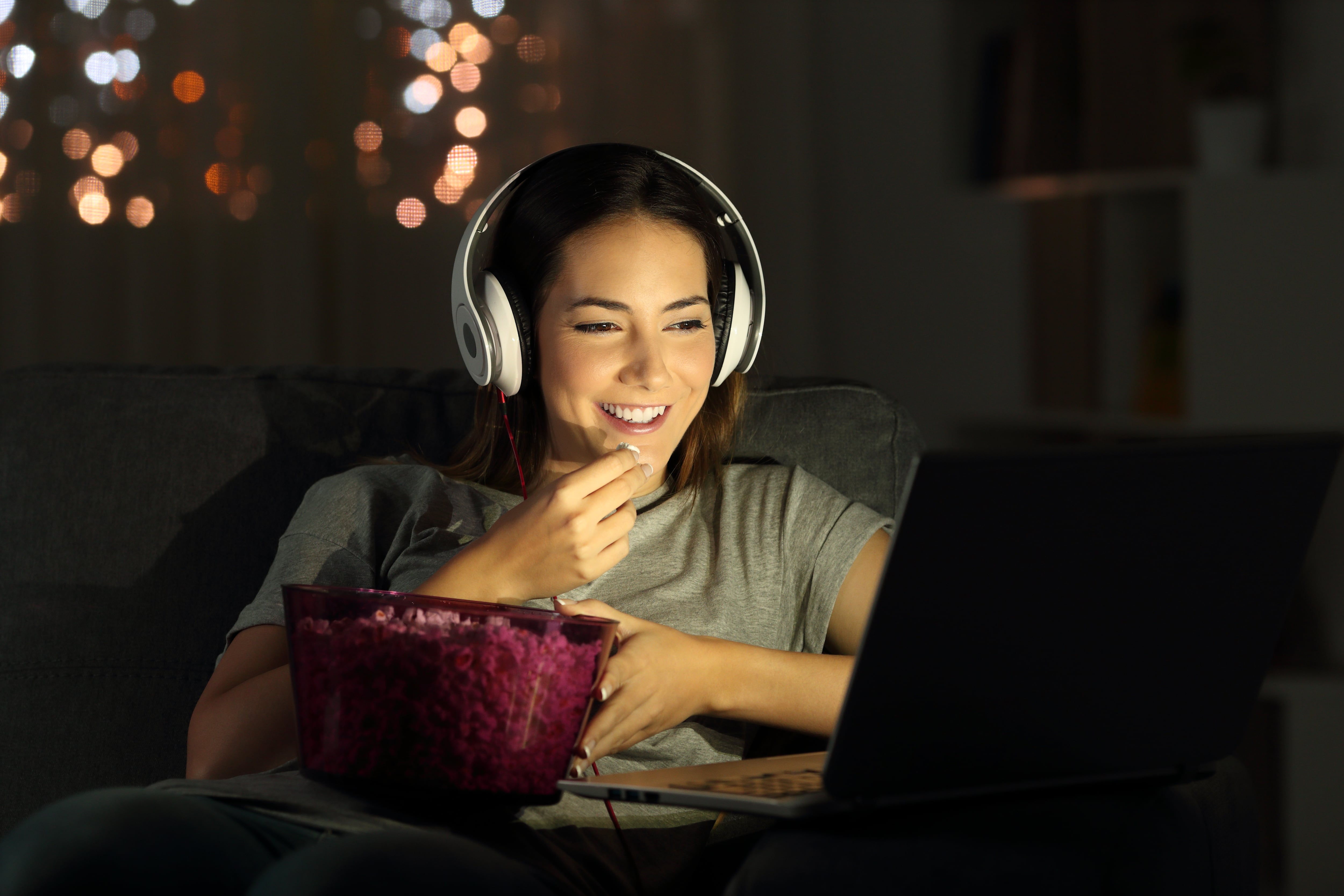Mujer viendo películas en su computador y comiendo palomitas de maíz (Foto vía Getty Images)