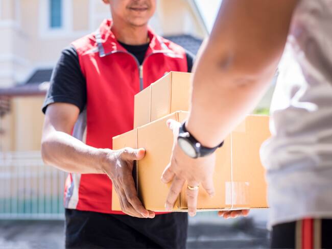 parcel delivery man of a package through a service and customer hand accepting a delivery of boxes from delivery man.