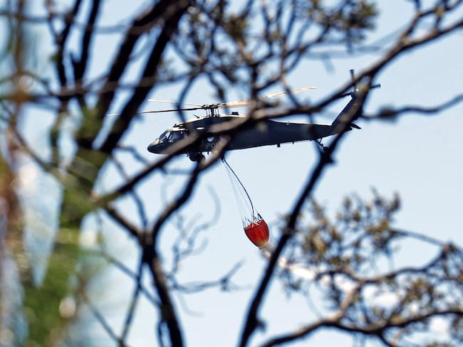 AME2250. BOGOTÁ (COLOMBIA), 25/01/2024.- Fotografía de un helicóptero mientras hace una descarga de agua en la zona de un incendio forestal hoy, en el cerro El Cable, en Bogotá (Colombia). Un total de 31 incendios forestales están activos este jueves en Colombia y afectan a nueve departamentos y Bogotá, donde sigue la emergencia por los fuegos en dos de sus cerros, informó este jueves la Unidad de Nacional de Gestión del Riesgo de Desastre (Ungrd). Los más preocupantes son precisamente los de los cerros orientales y El Cable de Bogotá, pues el humo se extiende por buena parte de la capital y está afectando la calidad del aire y las operaciones aéreas. EFE/ Mauricio Dueñas Castañeda