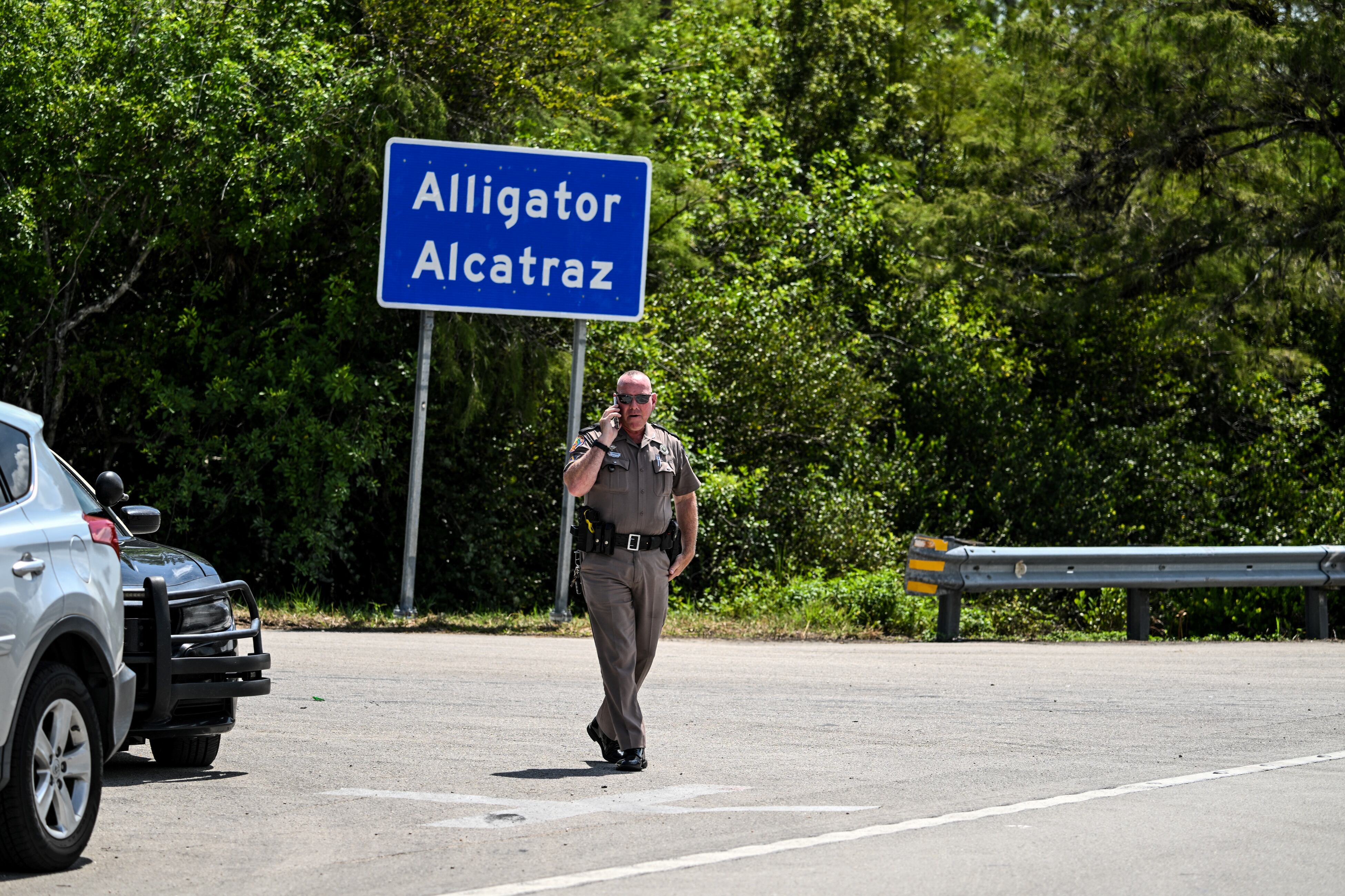 Un agente de la Patrulla de Carreteras de Florida observa mientras los manifestantes se reúnen para exigir el cierre del centro de detención de inmigrantes conocido como "Alligator Alcatraz" en el Aeropuerto de Entrenamiento y Transición Dade-Collier en Ochopee, Florida, el 22 de julio de 2025. (Foto de CHANDAN KHANNA / AFP)