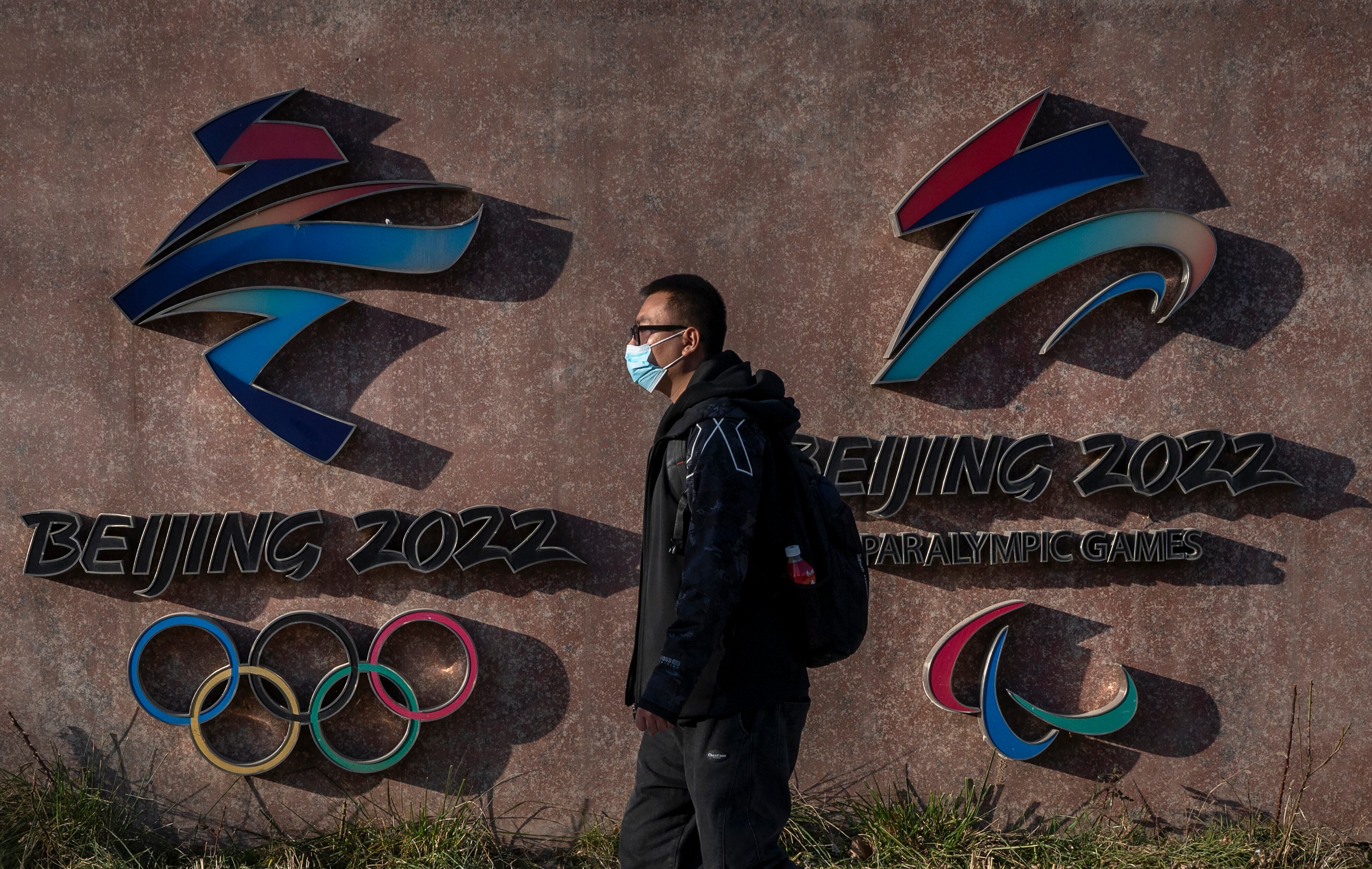 BEIJING, CHINA - DECEMBER 07: A visitor walks by the logos for the Beijing 2022 Winter Olympics and Paralympics at Shougang, a former power plant which now also houses the headquarters of the Beijing Organizing Committee of the Olympic Games, on December 7, 2021 in Beijing, China. The games are set to open on February 4, 2022.(Photo by Kevin Frayer/Getty Images)