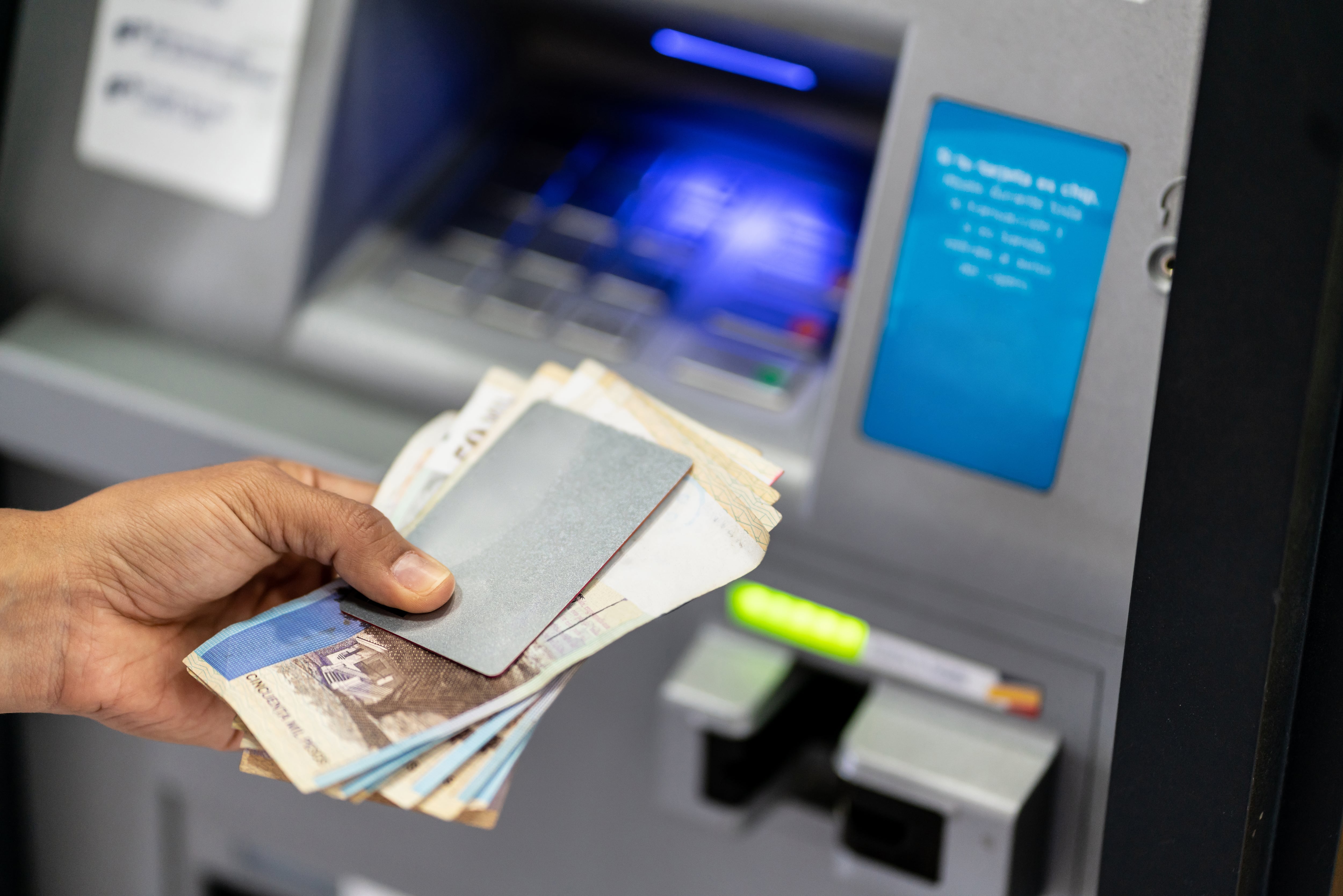 Unrecognizable man holding his debit card and cash after withdrawing from atm - Crad to edit