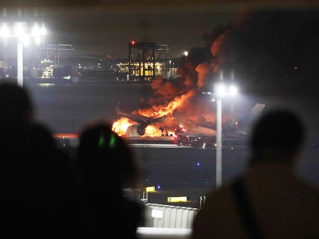 Tokyo (Japan), 01/01/2024.- People stand in a viewing platform as a Japan Airline passenger plane (rear) bursts into flames on the tarmac at Haneda Airport in Tokyo, Japan, 02 January 2024, after its landing. The JAL airplane apparently collided with a Japan Coast Guard plane as it landed. All 379 people on the JAL plane, including 367 passengers and 12 crew members, have been safely evacuated, according to JAL. The coast guard plane carried six crew members, one escaped from the aircraft and the others were unaccounred for, the coast guard said. (Japón, Tokio) EFE/EPA/JIJI PRESS JAPAN OUT EDITORIAL USE ONLY/