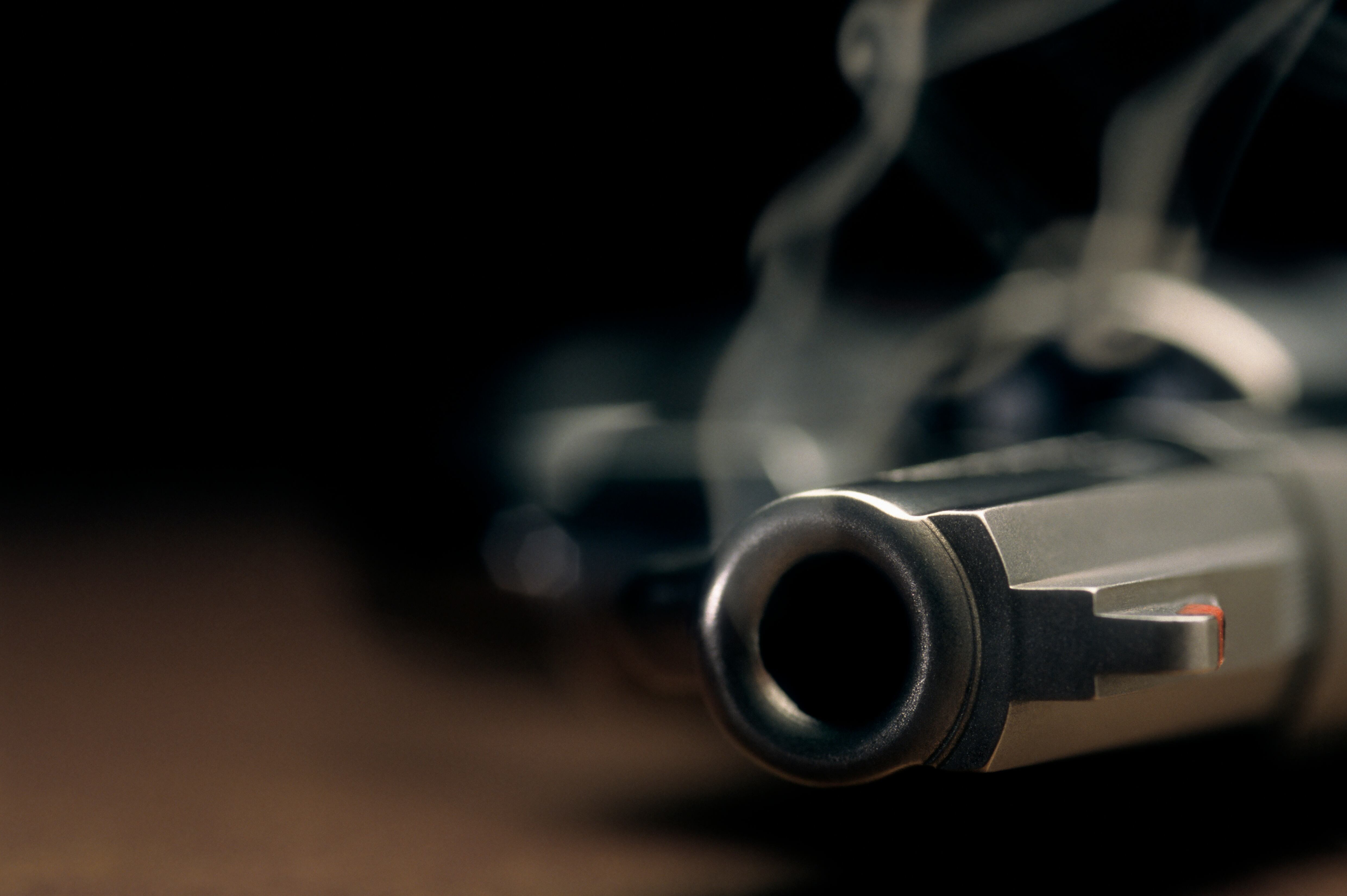 A gritty crime scene image of a smoking hand gun, revolver, lying on the floor with narrow focus on the tip if the barrel and dark background