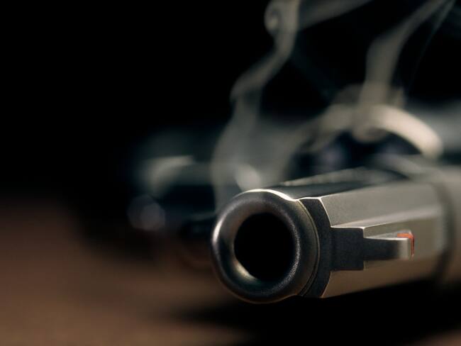 A gritty crime scene image of a smoking hand gun, revolver, lying on the floor with narrow focus on the tip if the barrel and dark background