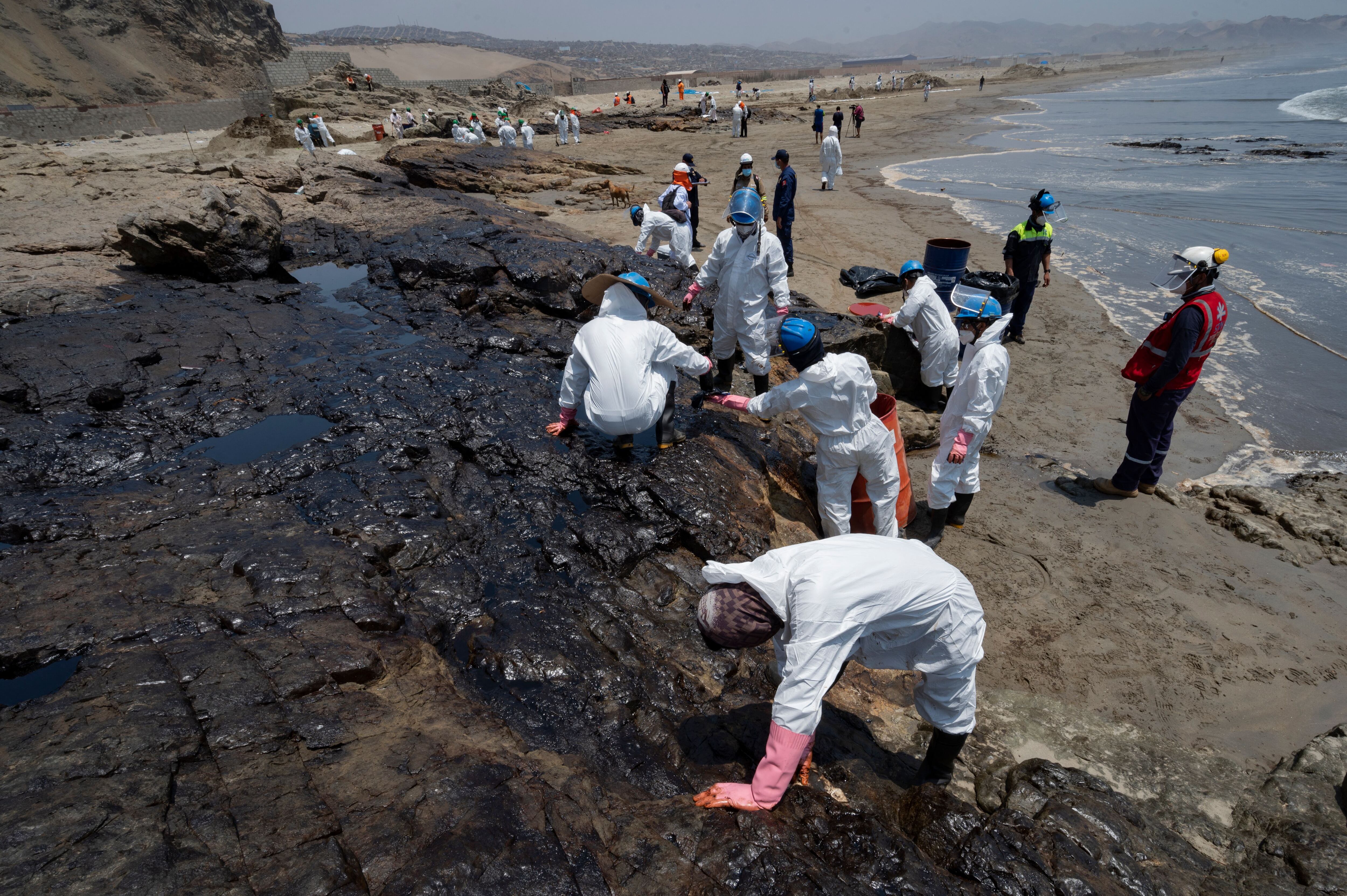 Cleaning crews work to remove oil from a beach in the Peruvian province of Callao on January 17, 2022, after a spill which occurred during the unloading process of the Italian-flagged tanker "Mare Doricum" at La Pampilla refinery caused by the abnormal waves recorded after the volcanic eruption in Tonga. - A massive volcanic eruption in Tonga triggered tsunami waves around the Pacific, with waves strong enough to drown two women in Peru, more than 10,000 kilometres (6,000 miles) away. (Photo by Cris BOURONCLE / AFP) (Photo by CRIS BOURONCLE/AFP via Getty Images)